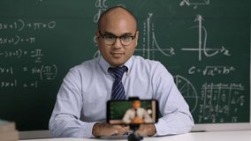 Indian young teacher man sitting teaching online video conference live stream by smartphone. Asian teacher teaching mathematics class webinar online for students learning.