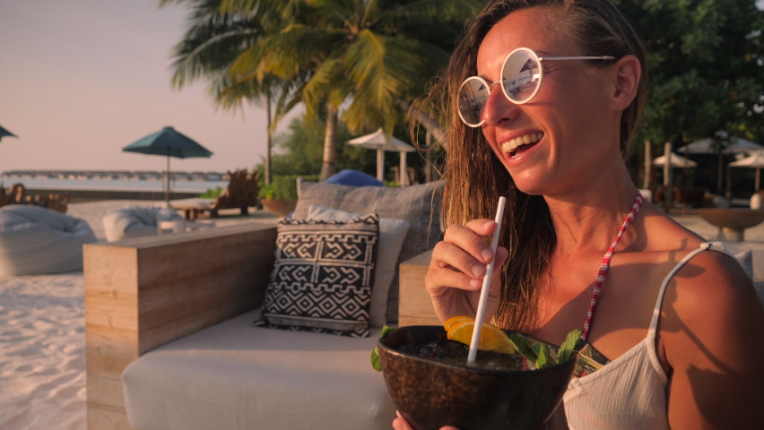 Woman having a cocktail at sunset on tropical beach. Young couple cheering and celebrating at a beach bar  Royalty-Free Stock Footage #1068284708