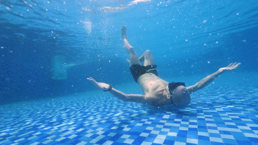 Young man lying on the bottom of the pool mastering to make bubble rings