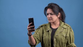 Young Asian Angry Woman making a video call talking on smartphone.annoyed woman having video call,working online meeting with team at studio indoor.Close up Portrait Angry Woman making a video call.