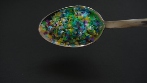 Microplastic in a spoon pours out on a black background.