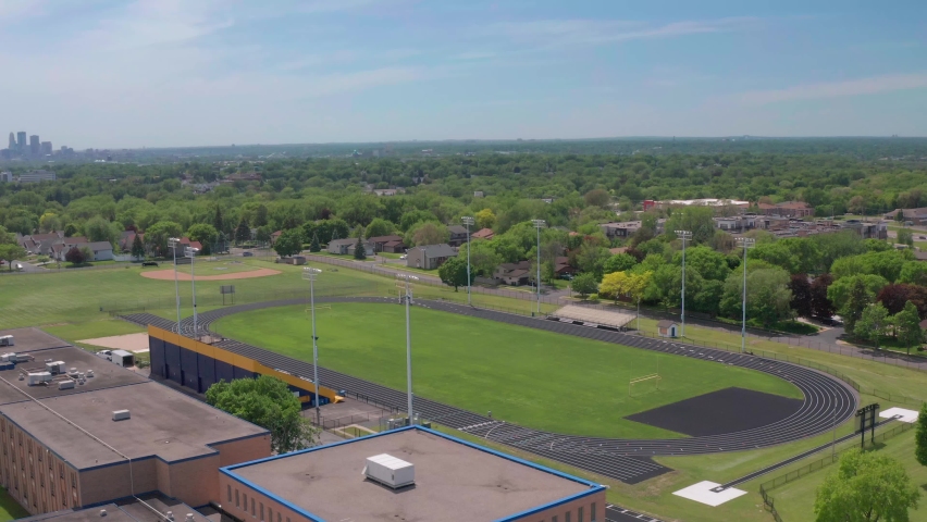 High school bleachers and track in residential neighborhood with city skyline on the horizon- aerial drone flyover shot
