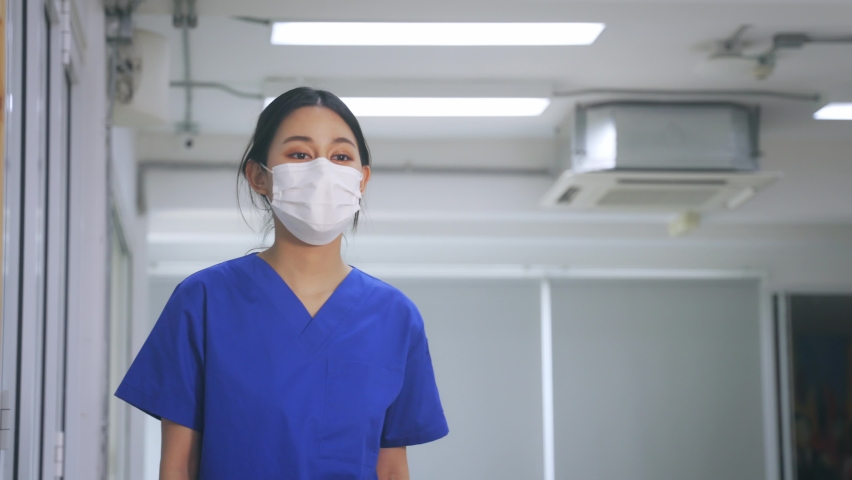 Young Asian nurse wearing scrubs uniform with surgical mask showing thumbs up sign and gesture while resuming to work and treat covid-19 infected patients in hospital. High quality 4k footage Royalty-Free Stock Footage #1068299159