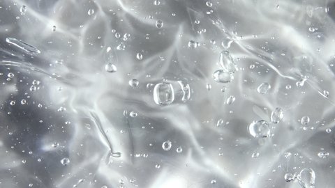 Transparent liquid gel background, clear serum texture. Motion, rotation of the beauty skincare product sample with bubbles. Top view. Macro Shot