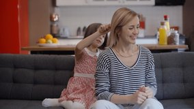 Little girl combing her mother's hair. Mother and daughter having fun, having a good time together. Portrait of happy and beautiful laughing family.Slow motion video.