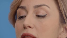 Make-up is wearing mascara on a woman with beautiful eyes. Close-up young woman's eyes. Blue background.Slow motion video.