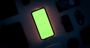 Phone chroma key green screen display mockup with tracking markers. Dark room interior with tech gadgets layout. Evening light scene with mobile illumination. Turning movement. 3D CGI close up 4k shot