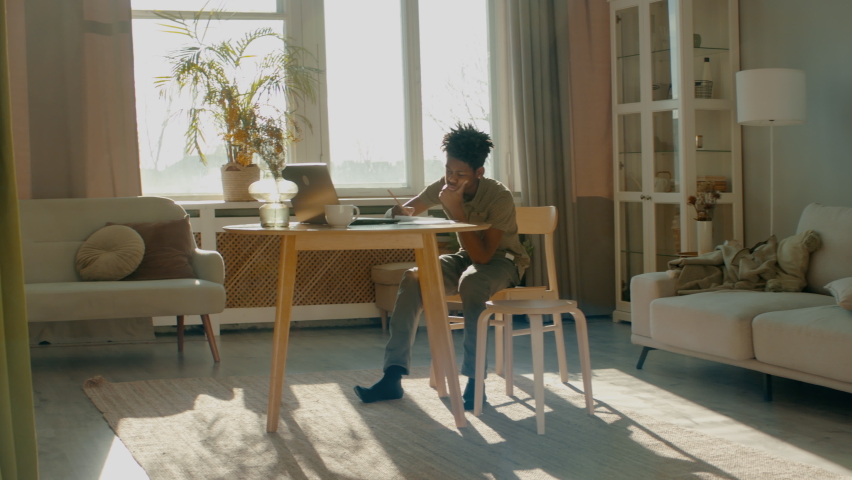 WIDE HANDHELD African American Black kid boy doing his homework or having a video call with class and teacher. Distance learning from home during isolation. Shot with 2x anamorphic lens