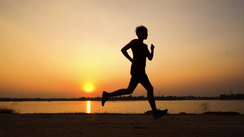 Silhouette, black shadow of slim male runner working out exercising alone. Man running and jogging training at beach sunset. Slow motion.
