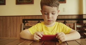 Portrait of a child looking at the phone, sitting at the table, a preschool kid uses artificial intelligence in a smartphone, baby boy watching a video on the phone.
