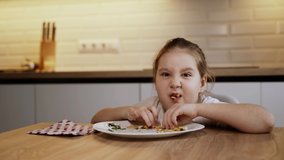 Very fun video. Cute girl devours french fries by two hands and and grimaces. The color of the kitchen facades is white. The girl is wearing a white T-shirt. 