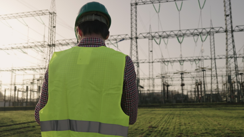 Electrical engineer wearing a helmet and safety vest working with tablet near high voltage electrical lines power station during sunset shot in 4k super slow motion Royalty-Free Stock Footage #1068325190