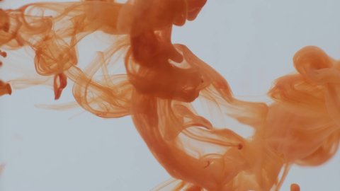 Movement of orange paint in the water, close-up. The paint dissolves in liquid. Colorful abstract shapes, close up