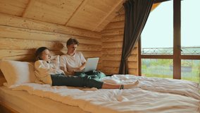 Happy young couple lying on bed in apartment and watching video on laptop with smile on face. Woman and young man watching movie on the bed in a country house.