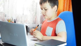 boy studies at home at the computer. remote education, school child learns lessons online using video broadcasting and modern technologies, looks at monitor screen and do homework, learning online