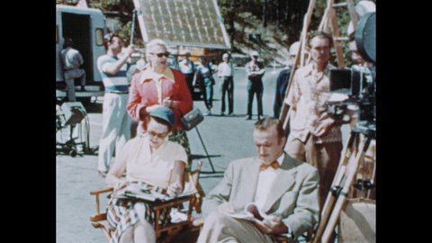 1950s: man and woman in canvas chairs write in scripts near movie crew, man stands, man with movie camera in back of convertible, woman enters passenger side of car, woman combs woman's hair