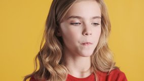 Close up beautiful blond teenage girl with wavy hair blowing bubble from gum on camera and happily smiling over yellow background. Funny girl blowing candy bubble
