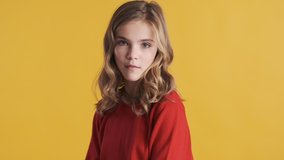 Attractive blond teenager girl dressed in red sweater dancing while posing on camera over yellow background