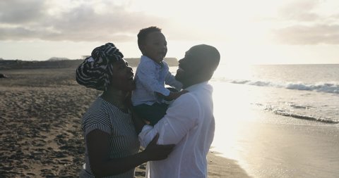 Cheerful african parents enjoy playful moment with little son on the beach outdoor - Family and love concept