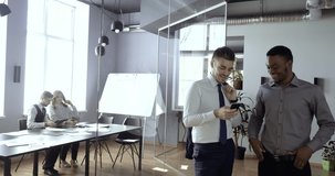 Two business colleagues talking at work relaxing looking at smartphone screen, background of managers routine. African american worker and caucasian man in office using phone to search net together - Powered by Shutterstock - Get 15% off with code: PIKWIZARD15