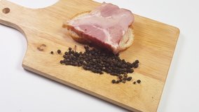 Slow motion 4 k video, cutting board with bread, ham and black pepper on white background.