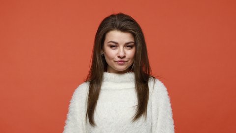 Curious nosy brunette woman in white fluffy sweater covering eyes with palm of hand, peeking through fingers, prying, looking with suspicion. Indoor studio shot isolated on orange background