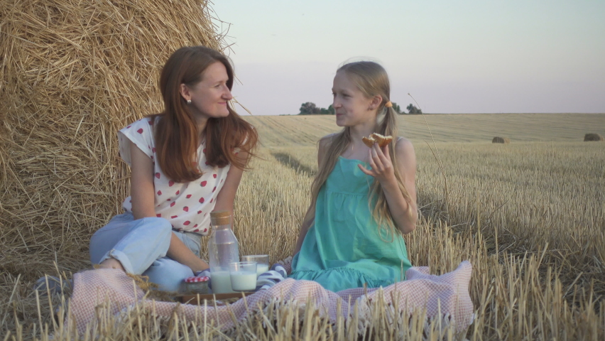 happy family in a wheat field. mother and daughter on a picnic in a wheat field near one of round bales at sunset time
