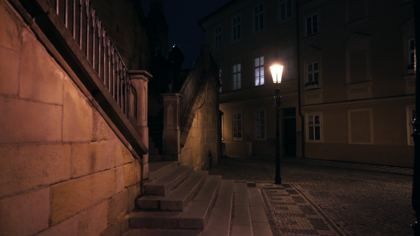 crossing the stairs from the 18th century and the street lights on Charles Bridge and the street lighted lantern of the night in the center of Prague. Royalty-Free Stock Footage #1068342992