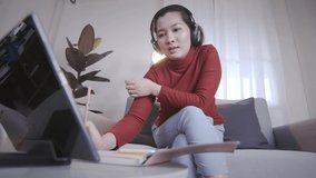 Asian woman on redshirt using a tablet with headphone for meeting online at home