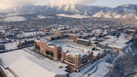 Aerial forward reveal of University of Colorado Boulder campus covered in snow on a winter morning with the mountains of the front range covered in clouds in the background