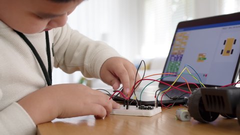 Young asia student remotely learn online at home in coding robot car and electronic board cable in STEM, STEAM, mathematics engineering science technology computer code in robotics for kids concept.