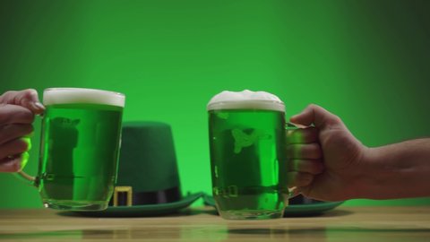two mugs of green frothy beer clink on a green background St. patrick's day