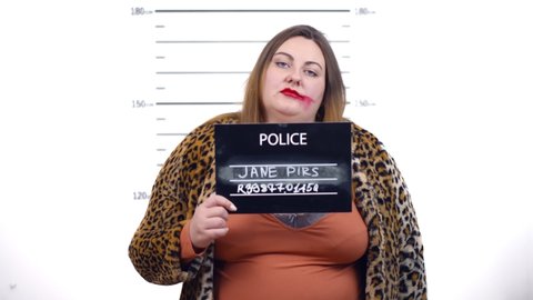 In police station arrested fat woman prostitute get front-view mug shot. Overweight hooker with heavy makeup holding placard with height chart on background