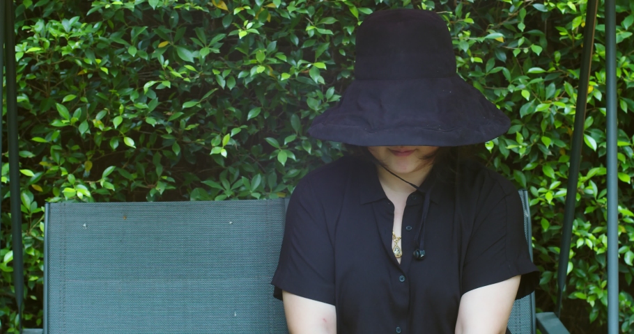 Portrait Asian cute young woman wearing black hat sitting on swings at the park against greenery nature plant background