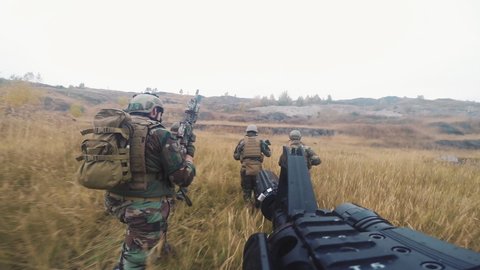 Point-of-view shot of squad of soldiers in camouflage uniform running through field armed with sniper rifles and guns