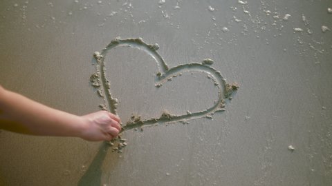close up female Woman hand drawing heart on sand by the beach and wave clear off the heart on the shore travel cocnept.