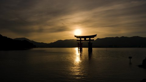 Hiroshima , Japan - 05 16 2016: Silhouette Miyajima Itsukushima Torii Gate Golden Yellow Sunset Timelapse. Locked Off