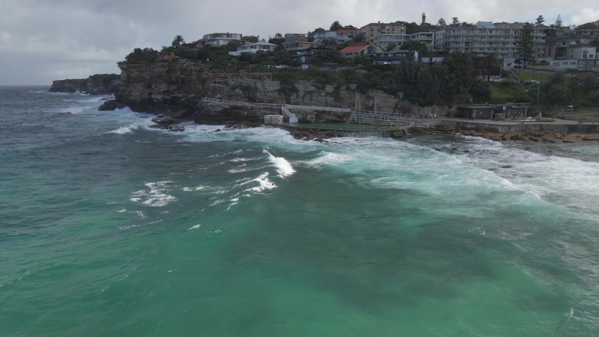 Waves Crashing On The Sea Wall Of Bronte Baths. Bronte Beach In Sydney, NSW, Australia. aerial sideways