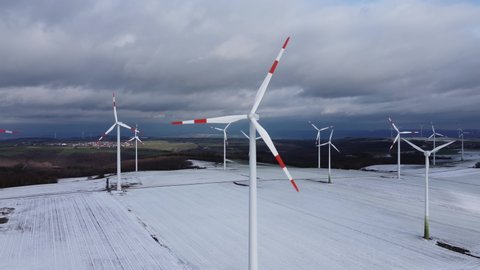 Aerial orbiting view of a wind farm in rural winter landscape during cloudy day outdoors in nature. Climate change