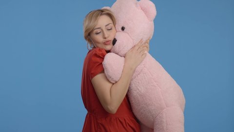 Young woman talking, hugging and kissing with a big teddy bear.Indoor studio shot isolated on blue background.