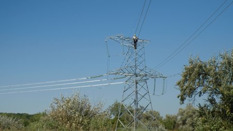 Skilled worker installs aviation marker balls fastened to wires of power transmission lines above green trees low angle shot