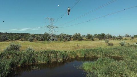 Technician installs bird flight diverters fastened to cables of electricity transmission lines above pond on sunny day upper view