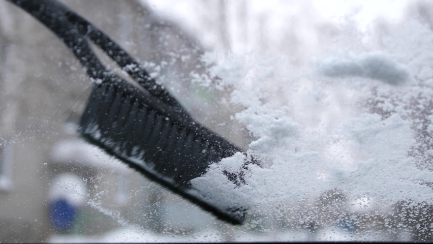 Sweep snow from the car. Car covered by snow after a snow blizzard. Men hands cleans the car from the snow, the view from inside the car. Cockpit view.