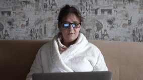 Old woman in glasses having a video call on the laptop smiling and talking happily indoors in a cozy apartment. doctor video calling older patient