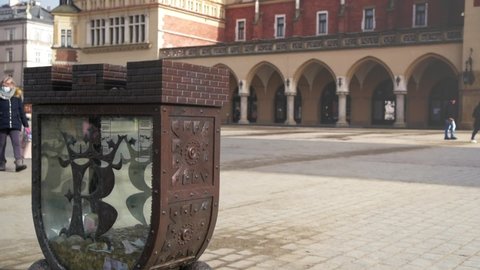 Krakow,Poland-February 2021: Fragment of historic Main Market Square in Krakow with symbolic city's moneybox. In background ,family walk through old square in historic city day during covid19 pandemic.