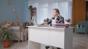 lesson online, happy elementary school student does homework with teacher via video communication and shows cards with letters in the screen of computer sitting at table in room