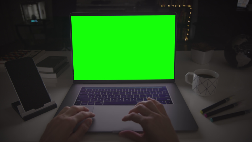 Laptop with green screen. Female hands clicking and scrolling on a track pad. Dark office. Locked. Royalty-Free Stock Footage #1068378065