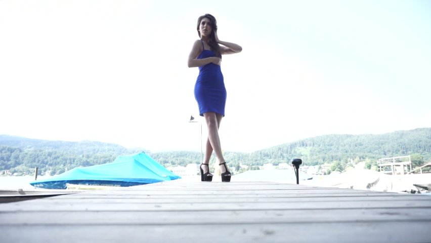 beautiful girl in blue short dress posing on the jetty of a lake