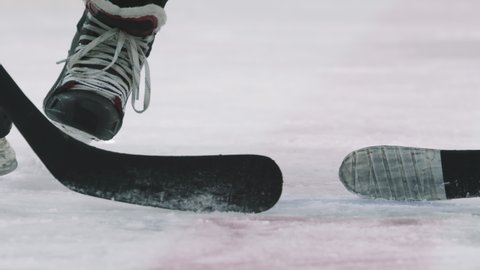 Slow-motion low-angle close up of hockey puck being dropped on ice and two unrecognizable male players from opposing teams start playing hockey