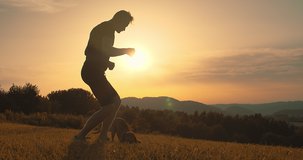 Silhouettes of runner and dog on field under golden sunset sky in evening time. Outdoor running. Athletic young man with his dog are running in nature. 4K video

